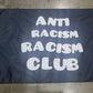 Black flag with 'Anti Racism Racism Club' text on a concrete floor.