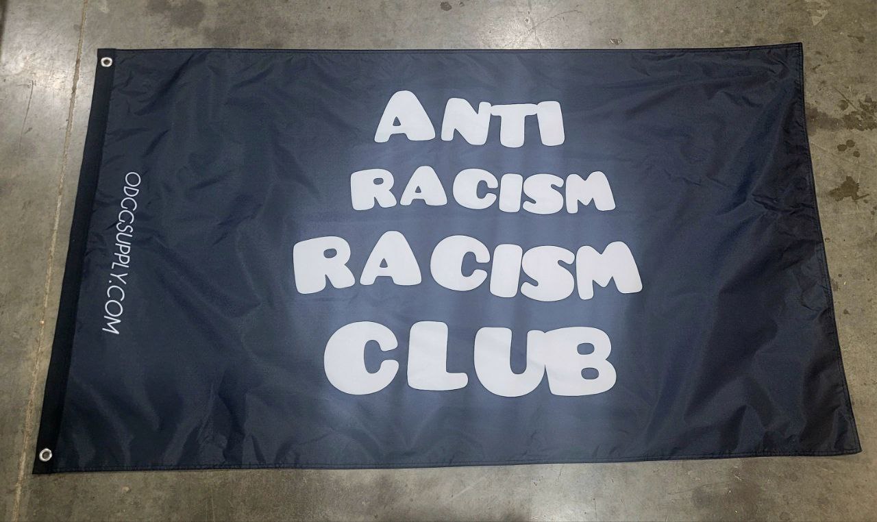 Black flag with 'Anti Racism Racism Club' text on a concrete floor.