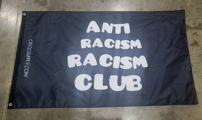 Black flag with 'Anti Racism Racism Club' text on a concrete floor.