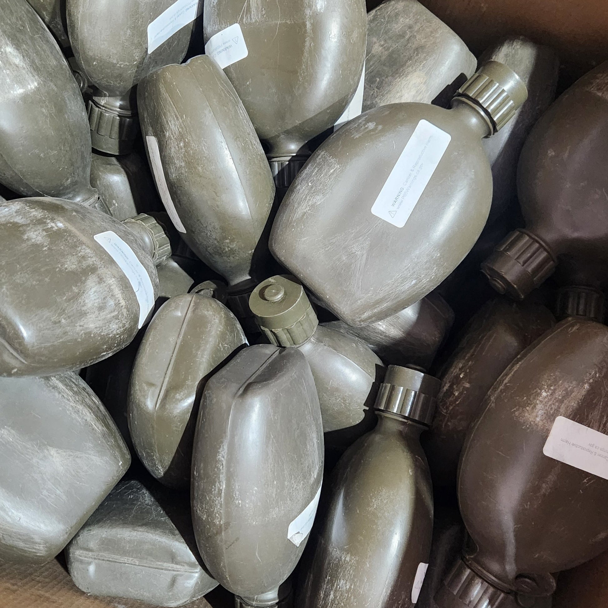 A group of military-style water bottles in olive drab and brown camouflage, packed inside a cardboard box with white labels attached.