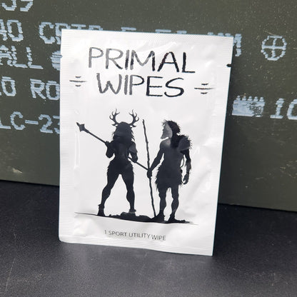 A white rectangular product package with black text reading 'PRIMAL WIPES' and a black graphic, placed on top of an olive green metal storage box against a dark gray surface.