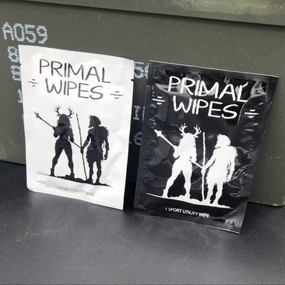 Two packs of Primal Wipes hand wipes, one black and one white, displayed on top of an olive green metal storage box against a dark gray background.