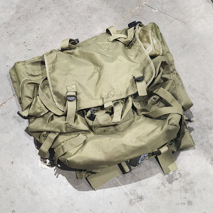 Green military-style backpack on a concrete floor with a person's foot visible.