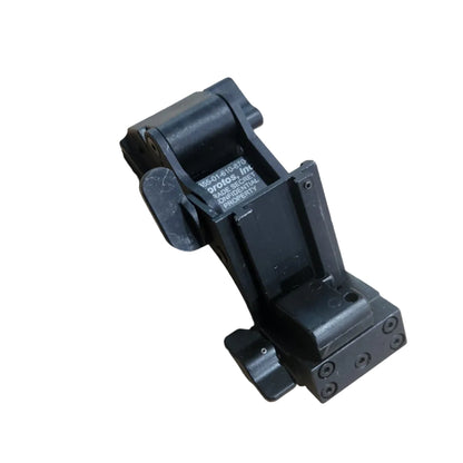 A black plastic mechanical component or bracket photographed on a tan cardboard surface.