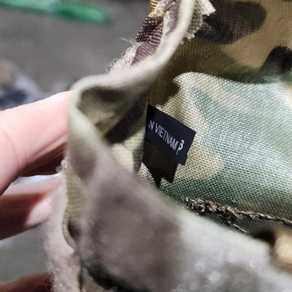 Close-up of a camouflage fabric with a visible brand label, held by a hand.