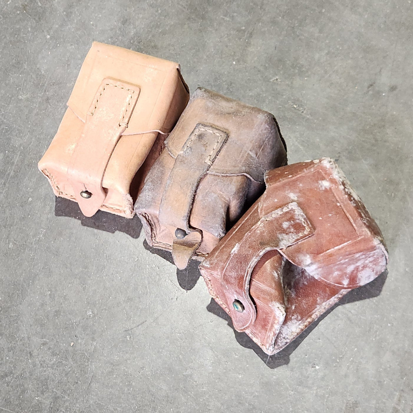 Leather pouches of varying conditions on a concrete floor