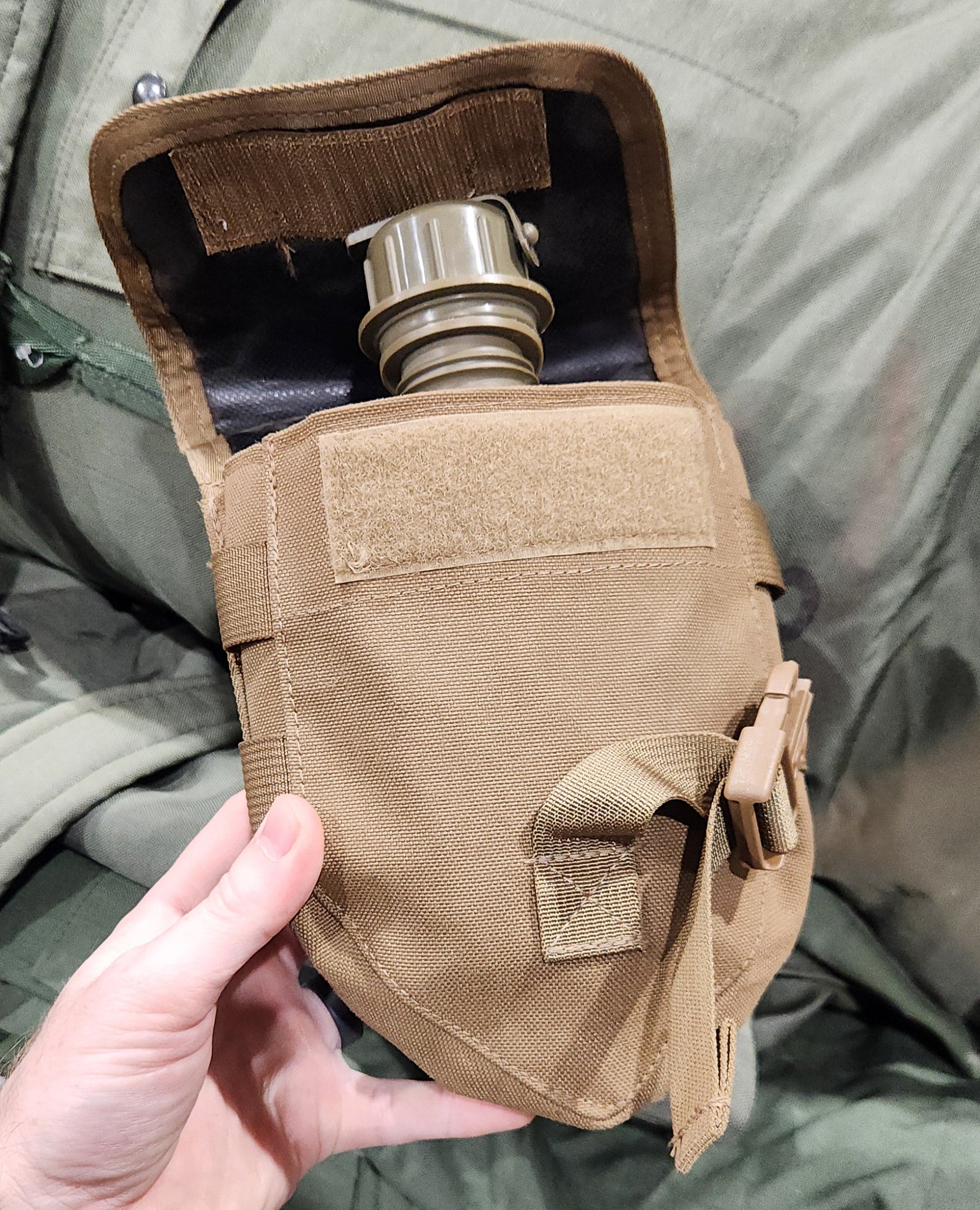 Person holding a tactical gas mask pouch with a gas mask inside, on a green military-style background.