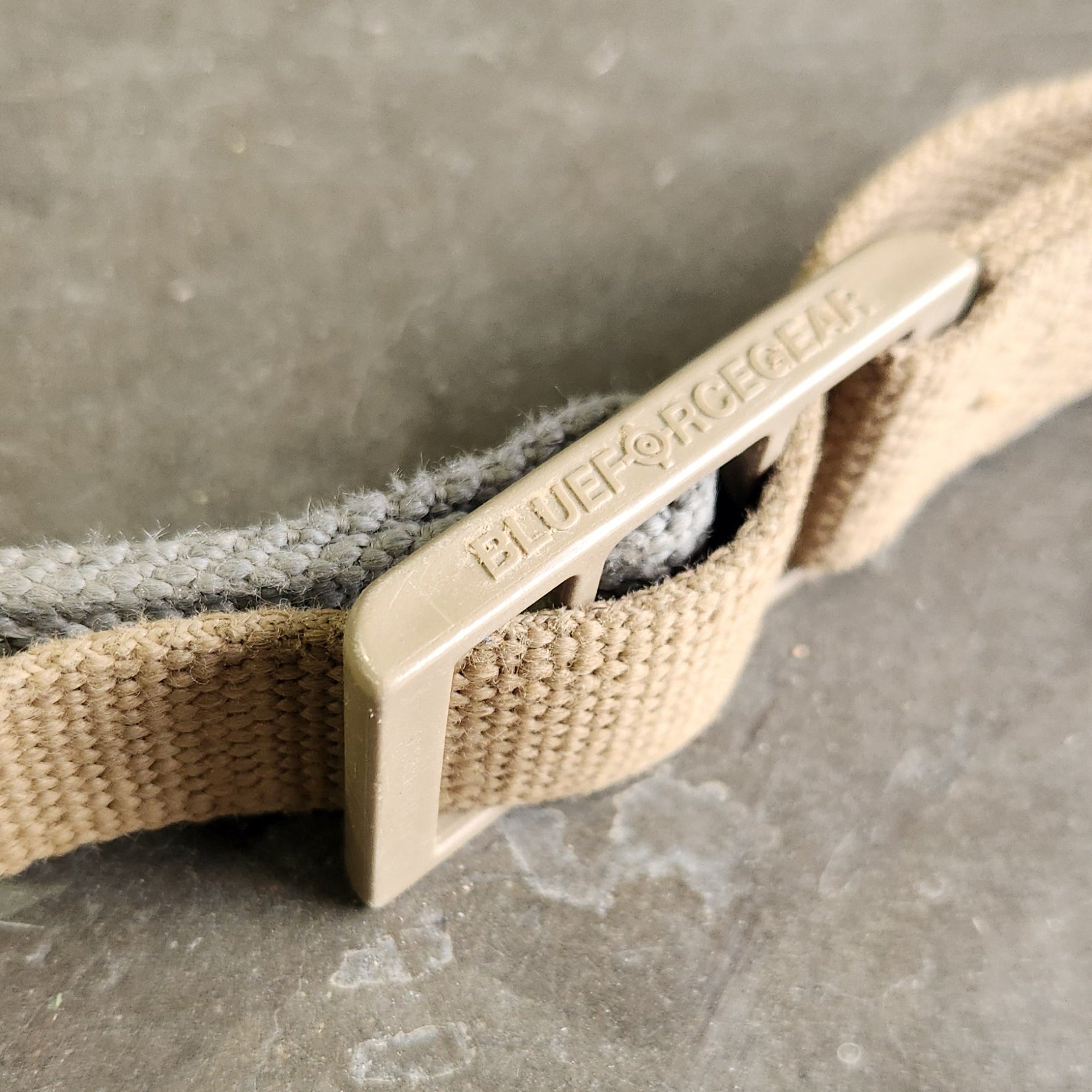 Close-up of a beige strap with a metal buckle on a textured gray surface
