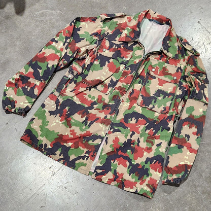 Camouflage-patterned jacket on a concrete floor with shoes and greenery in the background