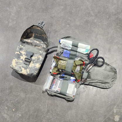 Assorted items including a bottle, scissors, and a camouflage-patterned bag on a concrete floor.