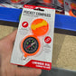 Orange pocket compass in packaging held by a hand with a store shelf in the background