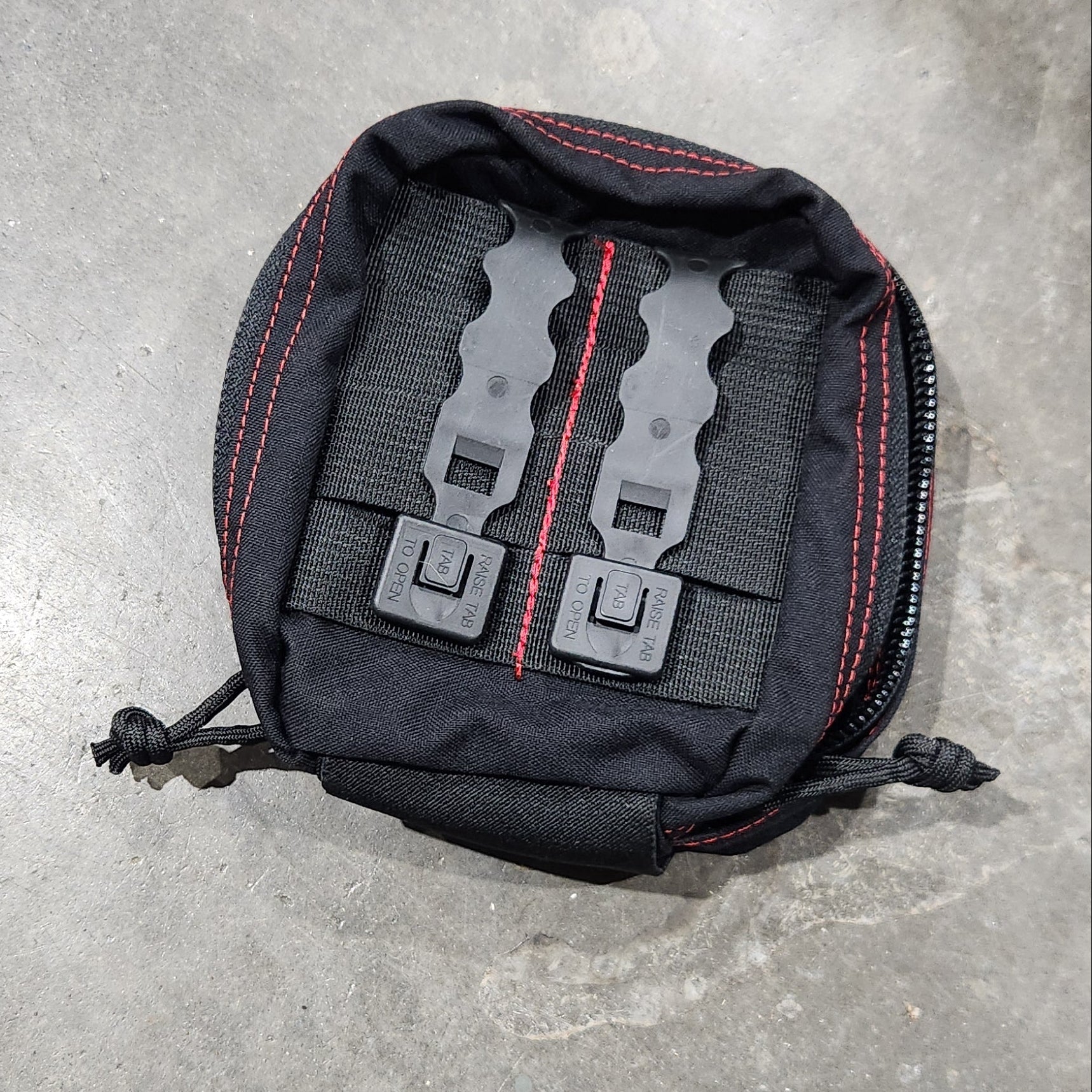 Black tactical pouch with visible branding on a gray concrete surface
