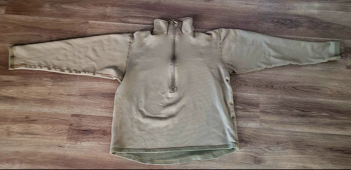 A light brown quarter-zip pullover sweater laid flat on a brown wood floor.