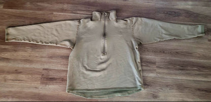 A light brown quarter-zip pullover sweater laid flat on a brown wood floor.