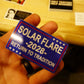 Hand holding a blue and red sticker with text 'Solar Flare 2028 Return to Tradition' against a blurred background.