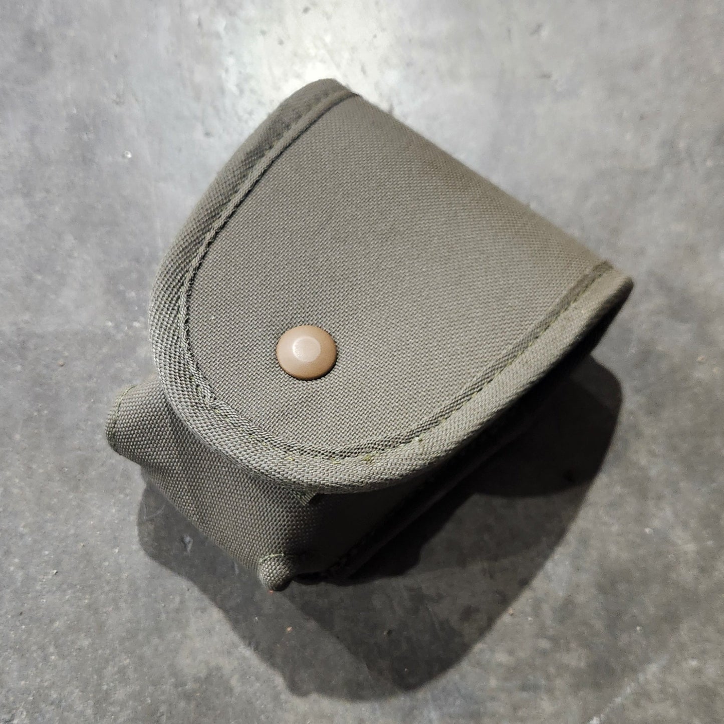 Small green fabric pouch with a button on a concrete surface