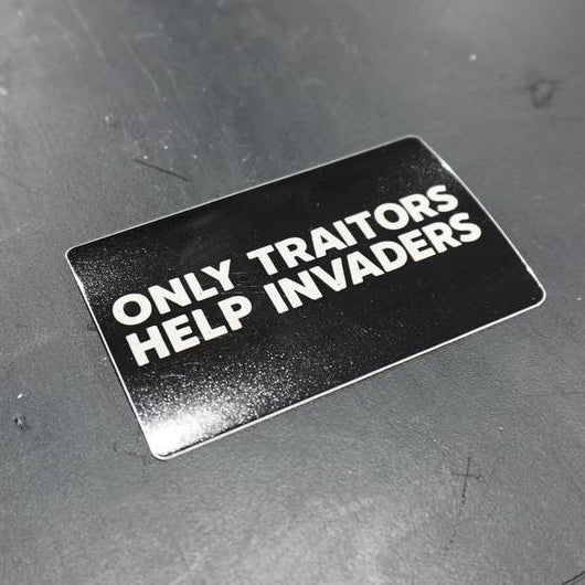 Sticker with text 'Only traitors help invaders' on a dark surface